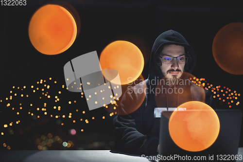 Image of hacker using laptop computer while working in dark office