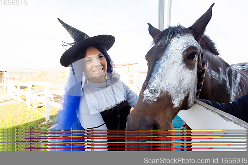 Image of A girl dressed as a witch shows the face of a horse painted with white paint for the holiday of halloween