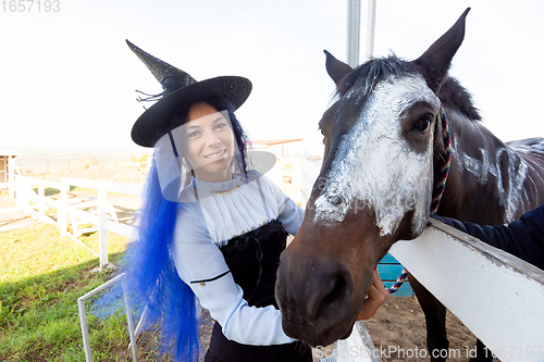 Image of A girl dressed as a witch shows the face of a horse painted with white paint for the holiday of halloween