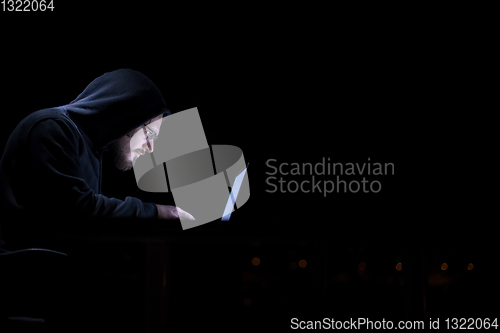 Image of hacker using laptop computer while working in dark office