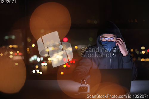 Image of hacker using laptop computer while working in dark office