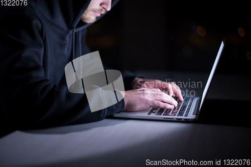 Image of hacker using laptop computer while working in dark office