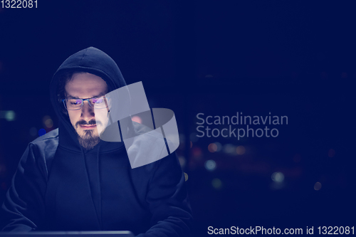 Image of hacker using laptop computer while working in dark office