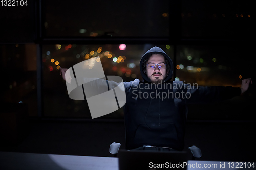 Image of hacker using laptop computer while working in dark office