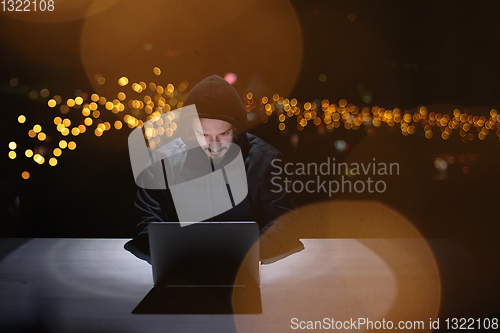 Image of hacker using laptop computer while working in dark office