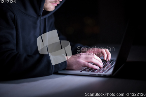 Image of hacker using laptop computer while working in dark office