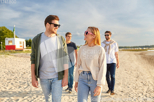 Image of happy friends walking along summer beach