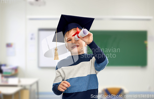 Image of little boy in mortarboard looking through diploma