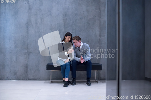 Image of business couple using mobile phone while sitting on the bench