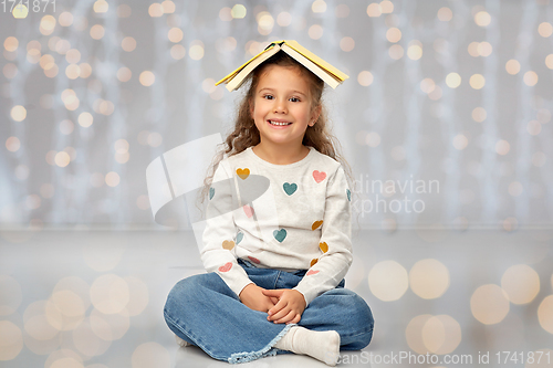 Image of portrait of smiling girl with book on head