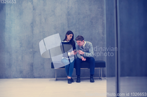 Image of business couple using mobile phone while sitting on the bench