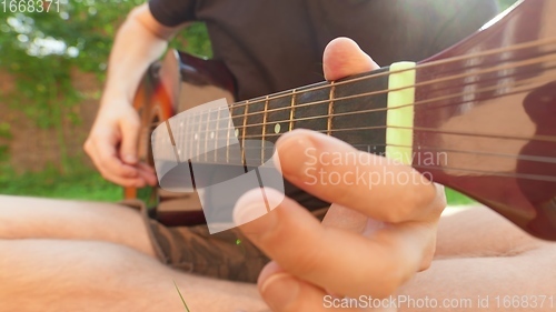 Image of Man sitting in the grass playing guitar