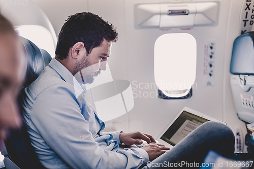 Image of Businessman working with laptop on airplane.