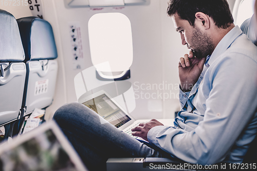 Image of Businessman working with laptop on airplane.