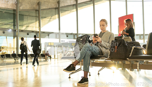 Image of Casual blond young woman using her cell phone while waiting to board a plane at airport departure gates.