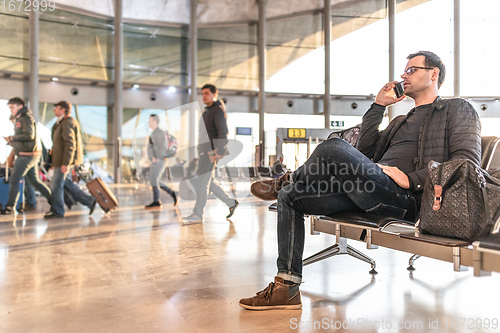 Image of Casual young male using her cell phone while waiting to board a plane at airport departure gates.