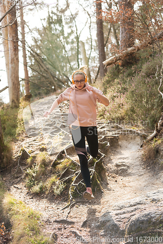 Image of Active sporty woman running in autumn fall forest jumping over the roots on the path. Healthy lifestyle image of young active caucasian woman jogging outside in nature