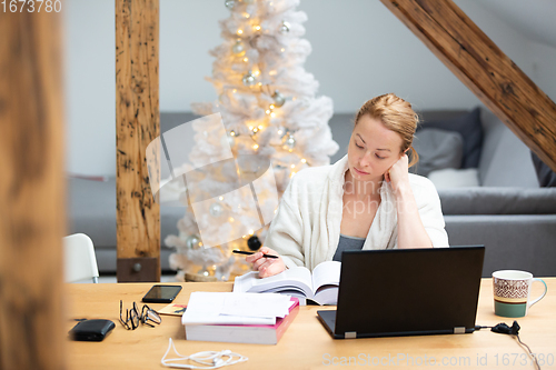 Image of Young female entrepreneur wearing cosy warm bathrobe working remotly from home in winter Christmas time during 2020 corona virus pandemic. Work from home, selter in place, concept.