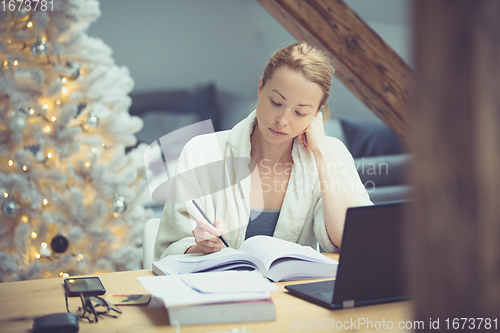 Image of Young female entrepreneur wearing cosy warm bathrobe working remotly from home in winter Christmas time during 2020 corona virus pandemic. Work from home, selter in place, concept.