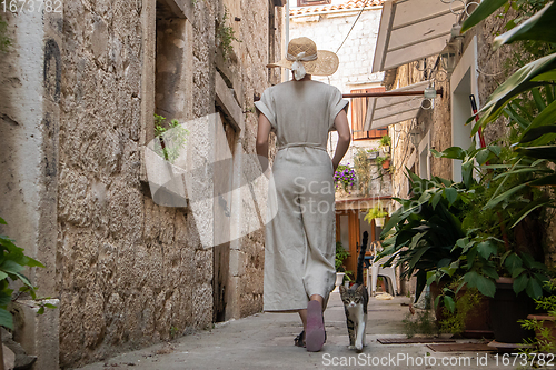 Image of Rear view of beautiful blonde young female traveler wearing straw sun hat sightseeing and enjoying summer vacation in an old traditional costal town at Adriatic cost, Croatia