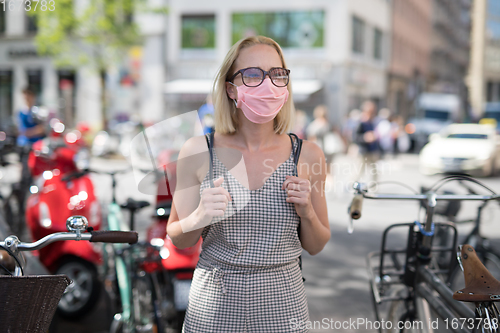 Image of Portrait of casual yound woman walking on the street wearing protective mask as protection against covid-19 virus. Incidental people on the background