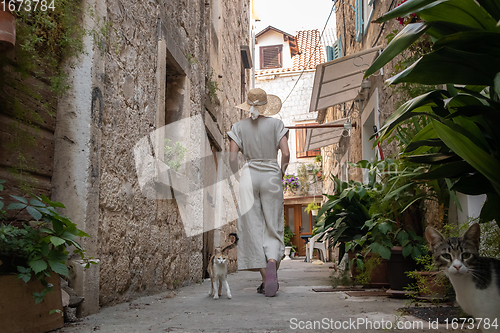 Image of Rear view of beautiful blonde young female traveler wearing straw sun hat sightseeing and enjoying summer vacation in an old traditional costal town at Adriatic cost, Croatia