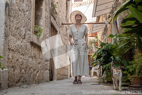 Image of Beautiful blonde young female traveler wearing straw sun hat sightseeing and enjoying summer vacation in an old traditional costal town at Adriatic cost, Croatia.