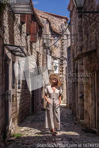 Image of Beautiful blonde young female traveler wearing straw sun hat sightseeing and enjoying summer vacation in an old traditional costal town at Adriatic cost, Croatia