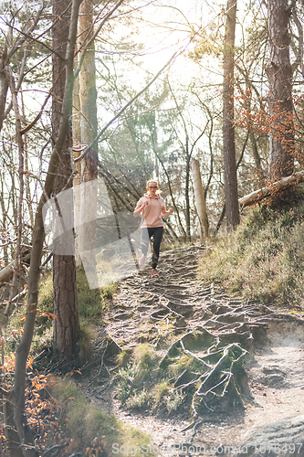 Image of Active sporty woman listening to the music while running in autumn fall forest. Female runner training outdoor. Healthy lifestyle image of young caucasian woman jogging outside