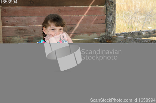 Image of Portrait of a beautiful girl of ten years old sitting at a wooden table in nature