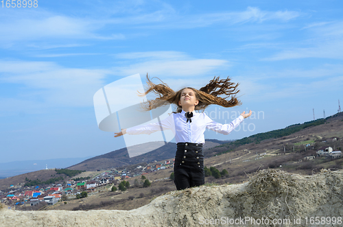 Image of Portrait of a beautiful girl of ten years old, with long developing hair in classic clothes against a background of blue sky and mountains