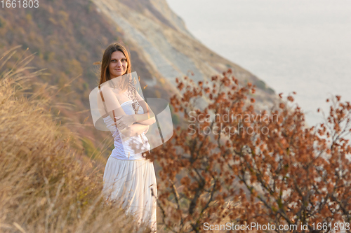Image of A beautiful girl stands on a rocky seashore and hugs wildflowers