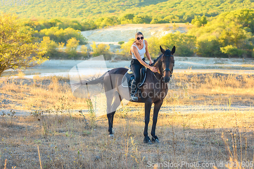 Image of Girl with glasses strokes a horse riding in the autumn forest