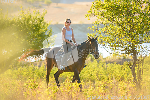 Image of A girl rides a horse on a warm autumn day