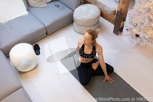 Image of Beautiful blonde woman doing home workout indoors. Woman practice yoga at home. Fit girl using workout tutorials for healthy active lifestyle. Woman using quarantine for home workouts.