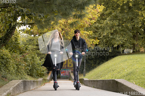 Image of Trendy fashinable teenagers riding public rental electric scooters in urban city park. New eco-friendly modern public city transport in Ljubljana, Slovenia