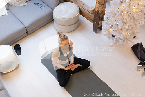 Image of Beautiful blonde woman doing home workout indoors. Woman practice yoga at home. Fit girl using workout tutorials for healthy active lifestyle. Woman using quarantine for home workouts.