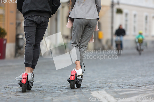 Image of Rear view of unrecognizable trendy fashinable teenagers riding public rental electric scooters in urban city environment. New eco-friendly modern public city transport in Ljubljana, Slovenia.