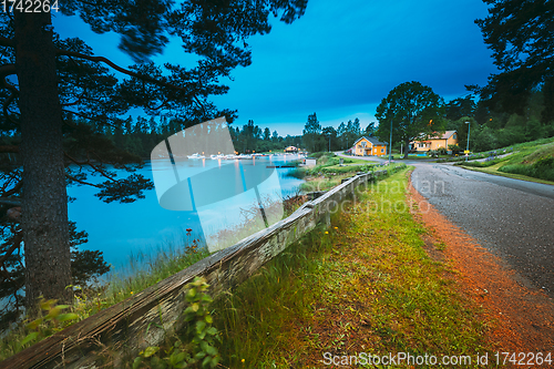 Image of Sweden. Road To Beautiful Swedish Village near Lake. Wooden Log Cabin Houses In Summer Evening Night. Lake Or River Landscape
