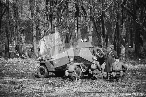 Image of Group Of Reenactors Dressed As Russian Soviet Red Army Soldiers Of World War II Go On Offensive Under Cover Of Armored Soviet Scout Car. Historical Reenactment In Forest