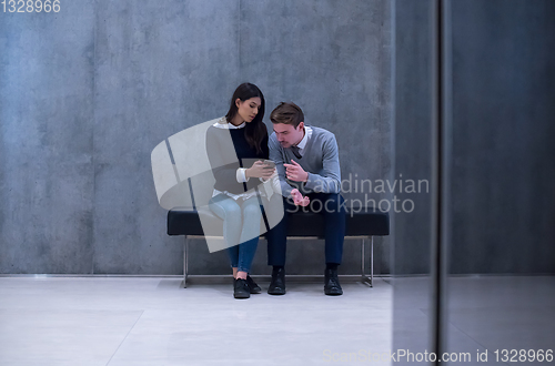 Image of business couple using mobile phone while sitting on the bench