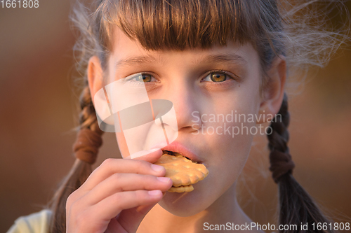 Image of Cute cheerful little girl is eating cookies at sunset, close-up