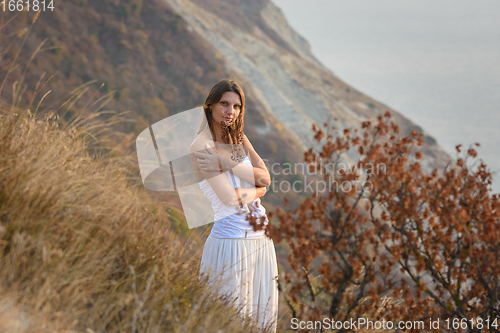 Image of A girl embraces wildflowers on the background of a beautiful mountain and sea landscape