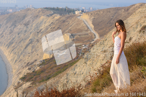 Image of A girl stands on a mountainside at sunset against a beautiful landscape