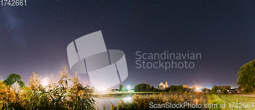 Image of Panorama Of Evaporation Over River Lake Near Houses In Village. Night Starry Sky Above Lake River With Bright Stars And Meteoric Track Trail. Glowing Stars Above Summer Nature