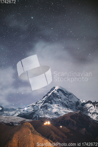 Image of Stepantsminda, Georgia. Night Starry Sky With Glowing Stars Above Peak Of Mount Kazbek Covered With Snow. Famous Gergeti Church In Night Lightning. Beautiful Georgian Landscape In Late Autumn