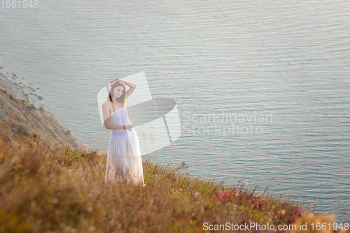 Image of A beautiful tall slender girl stands on a hill by the sea