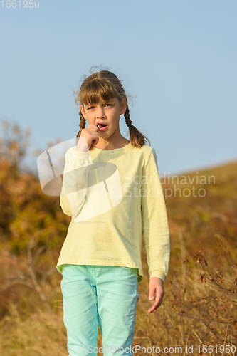 Image of The girl nibbles on a lollipop and looks at the frame with a puzzled look