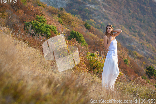 Image of A beautiful slender girl in white clothes stands on the mountainside