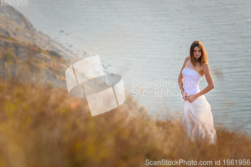 Image of A beautiful slender girl stands on a hillock against the background of the sea